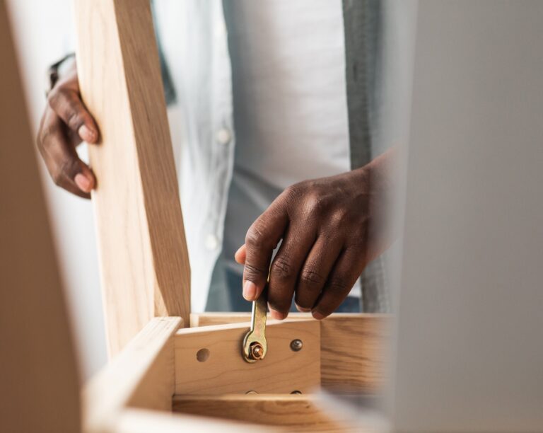 Carpentry concept. Black man assembling wooden table, screwing bolt with wrench, doing by yourself